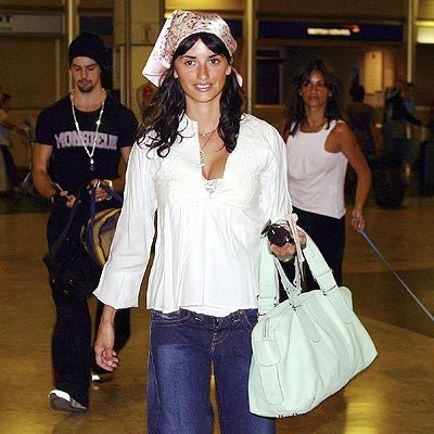 Woman in jeans and a white blouse carrying a pale green shoulder bag.