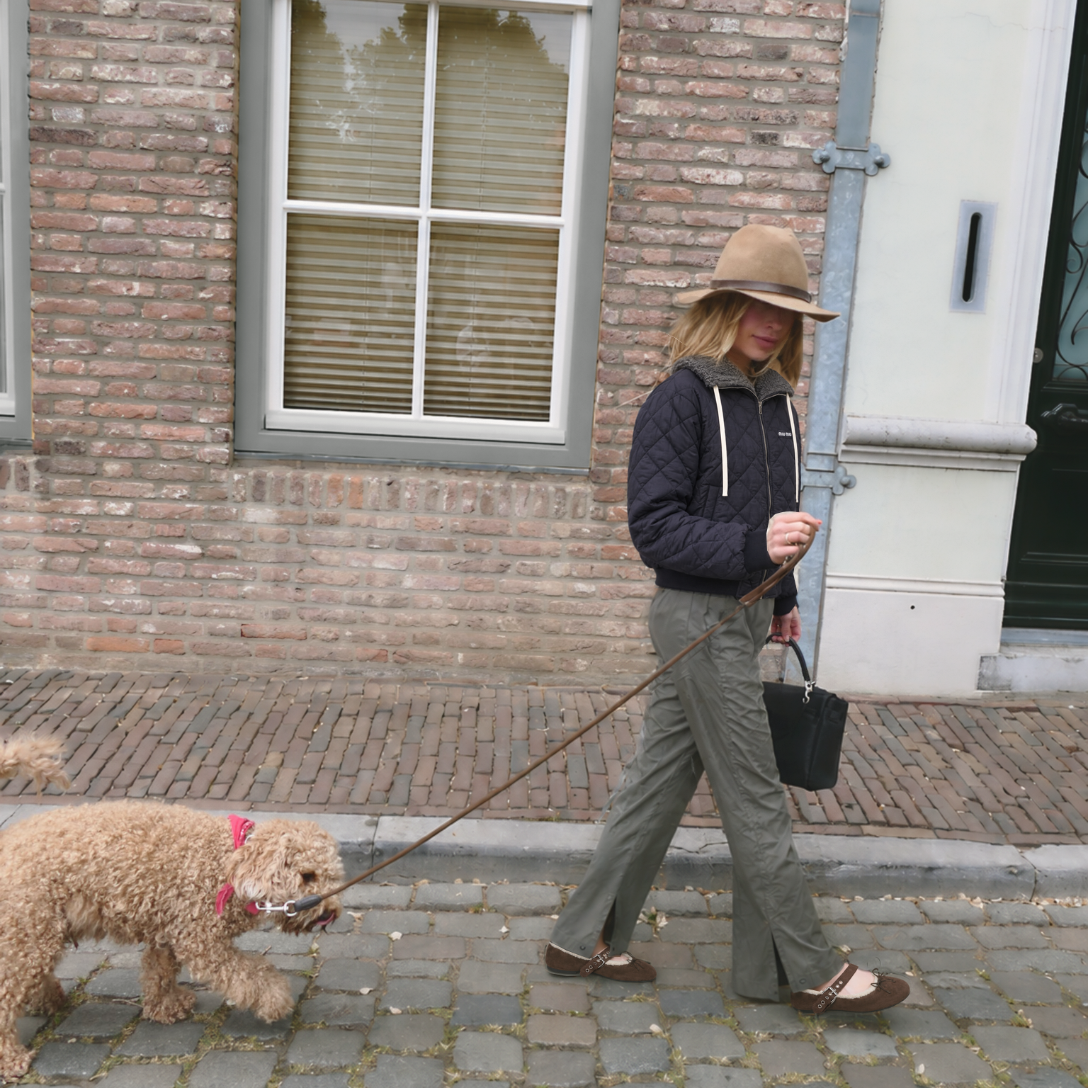 TII personal outfit photograph: quilted navy jacket, olive technical trousers and brown ballerinas while walking a dog on a cobbled street.