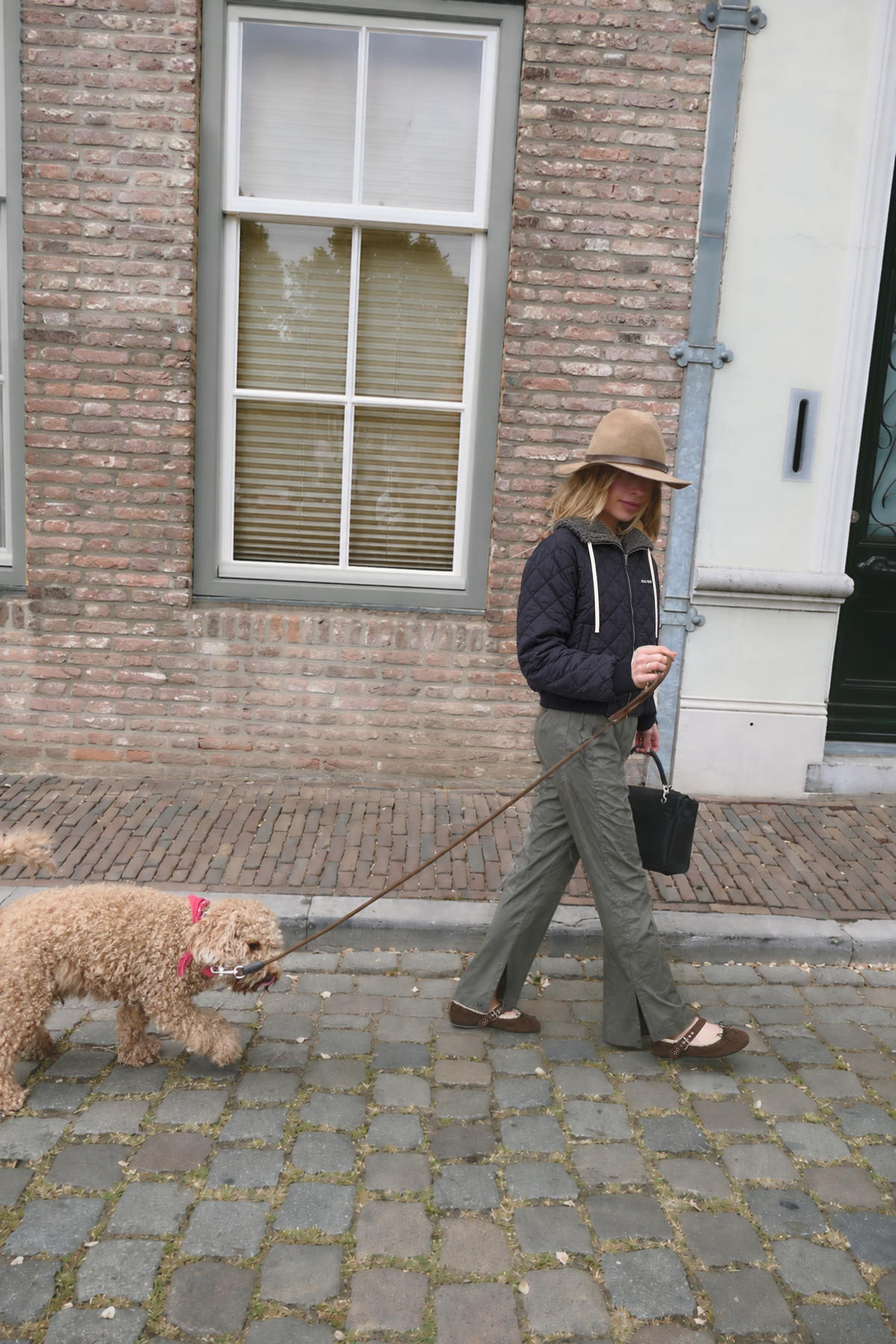 TII personal outfit photograph: quilted navy jacket, olive technical trousers and brown ballerinas while walking a dog on a cobbled street.