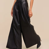 A person wearing a white sleeveless top and the Chelsy Leather Wide-Leg Pant, styled with black pointed-toe heels, poses against a beige background.
