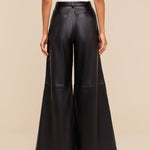 Wearing the Chelsy Leather Wide-Leg Pant in a high-rise, black lightweight leather, paired with a white sleeveless top, a person is pictured from the back against a plain beige background.