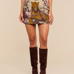 Wearing the Marseille Mini Skirt—vintage-inspired with a bold leopard and floral design—cinched at the waist with a brown belt and paired with knee-high brown suede boots, they stand against a neutral background.