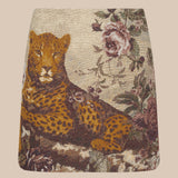 The Marseille Mini Skirt is a vintage-inspired mini skirt crafted from luxurious Italian jacquard, featuring a reclining leopard surrounded by pink and burgundy flowers on a beige background.