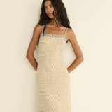 Woman wearing a beige patterned dress with blue trim against a plain background