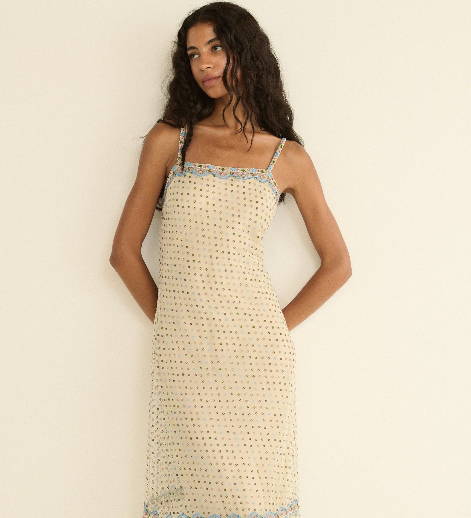 Woman wearing a beige patterned dress with blue trim against a plain background