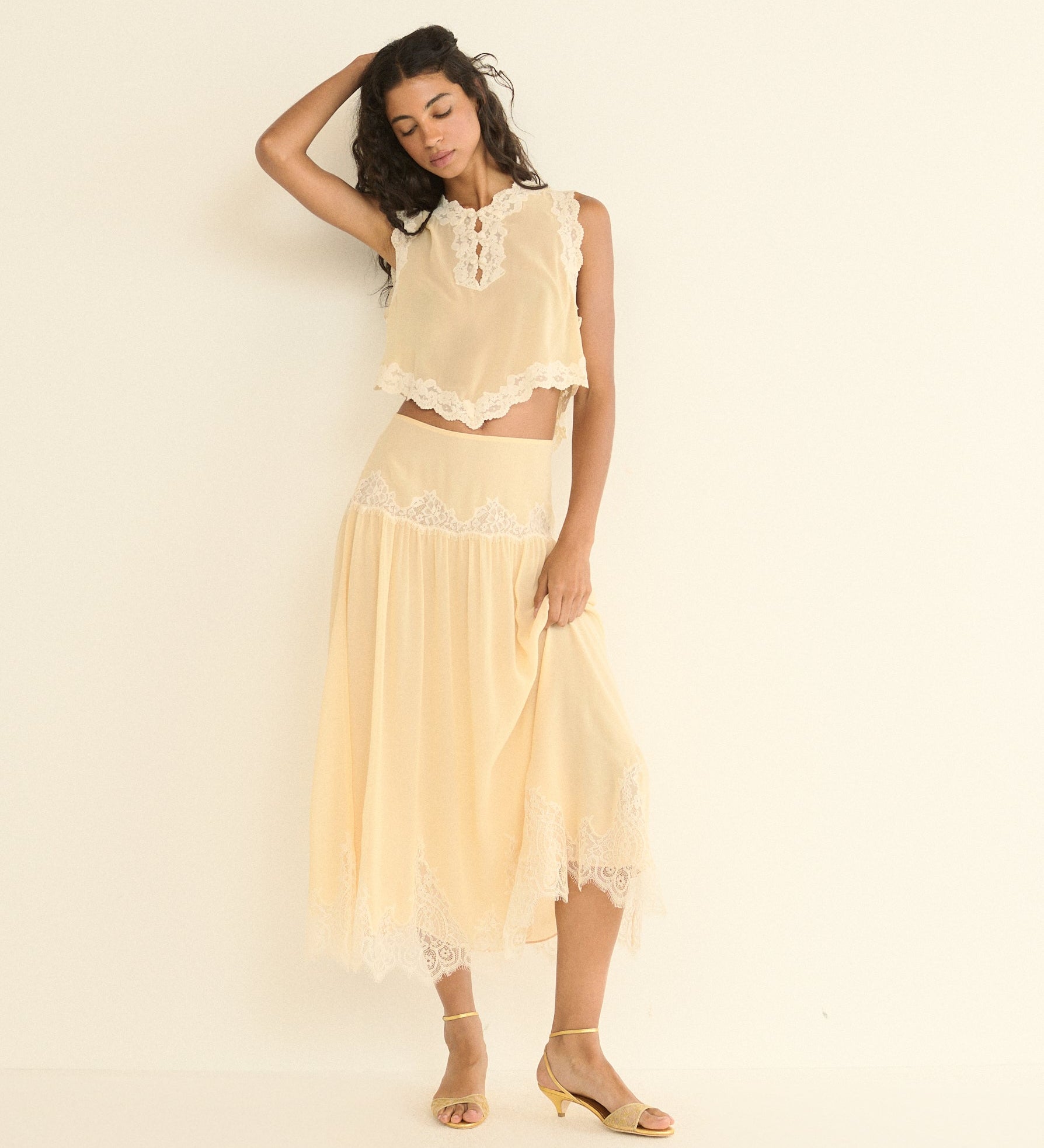 Woman wearing a light beige lace outfit against a plain background
