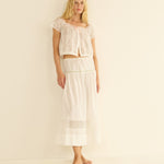 Woman wearing a white lace top and skirt set on a beige background