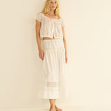 Woman wearing a white lace top and skirt set on a beige background