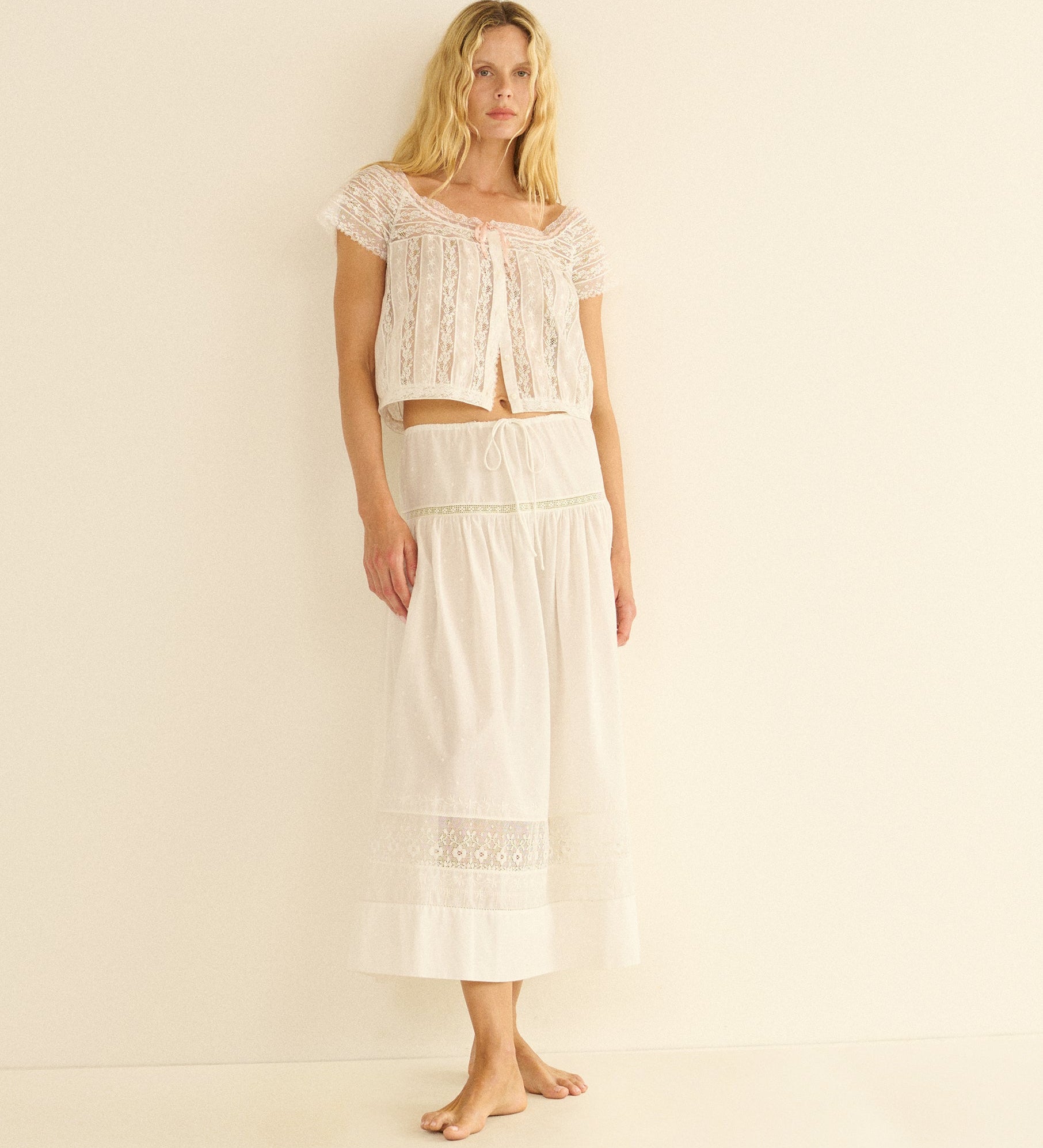 Woman wearing a white lace top and skirt set on a beige background