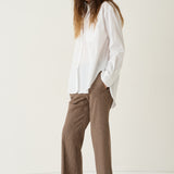A woman modeling a white long-sleeve button-up shirt and brown houndstooth cropped trousers with burgundy pointed-toe flats, set against a plain off-white studio background.