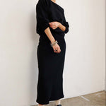 Person wearing a black outfit standing against a white wall.