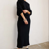 Person wearing a black outfit standing against a white wall.