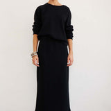 Person wearing a black outfit with a long skirt against a white background