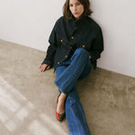 Woman sitting on a concrete floor wearing a dark jacket and blue jeans.