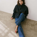 Woman sitting on a concrete floor wearing a dark jacket and blue jeans.