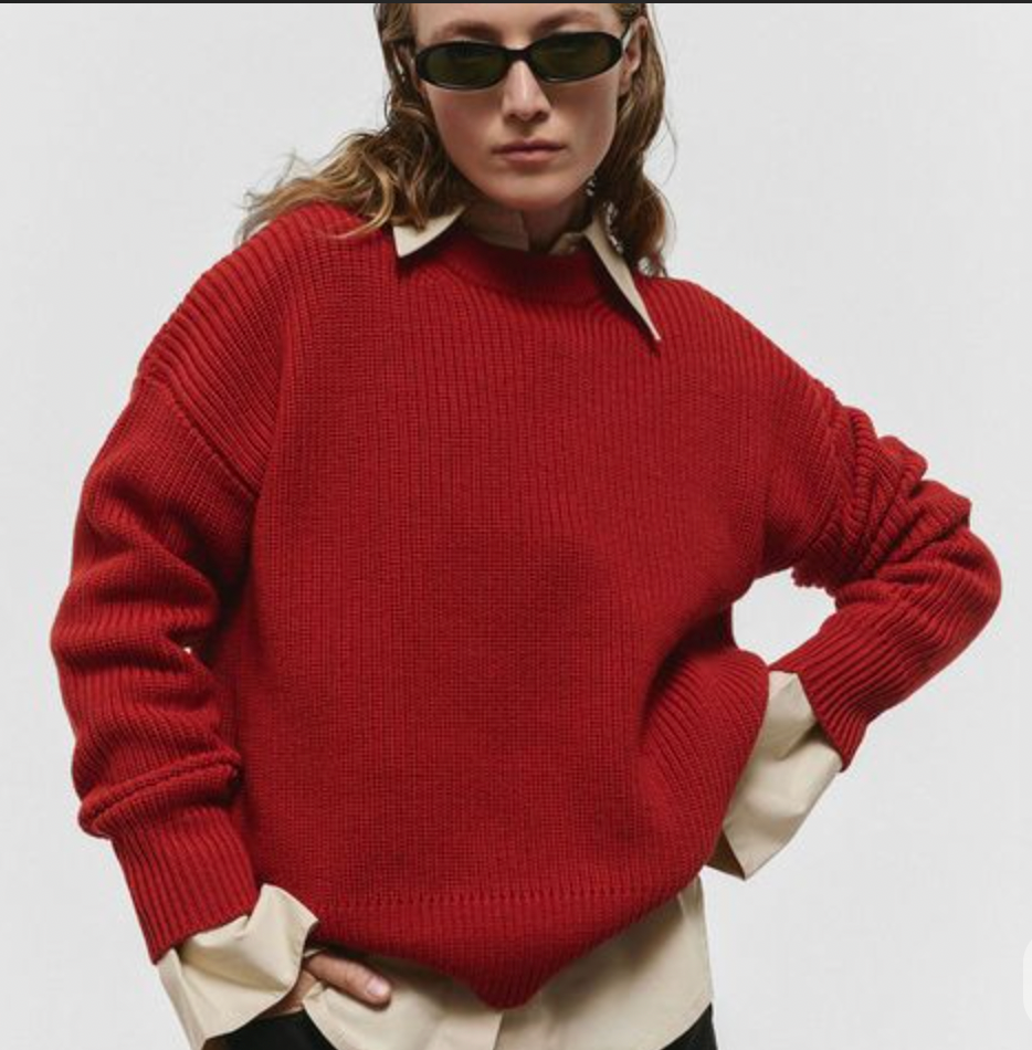 Person wearing a red sweater and sunglasses on a plain background