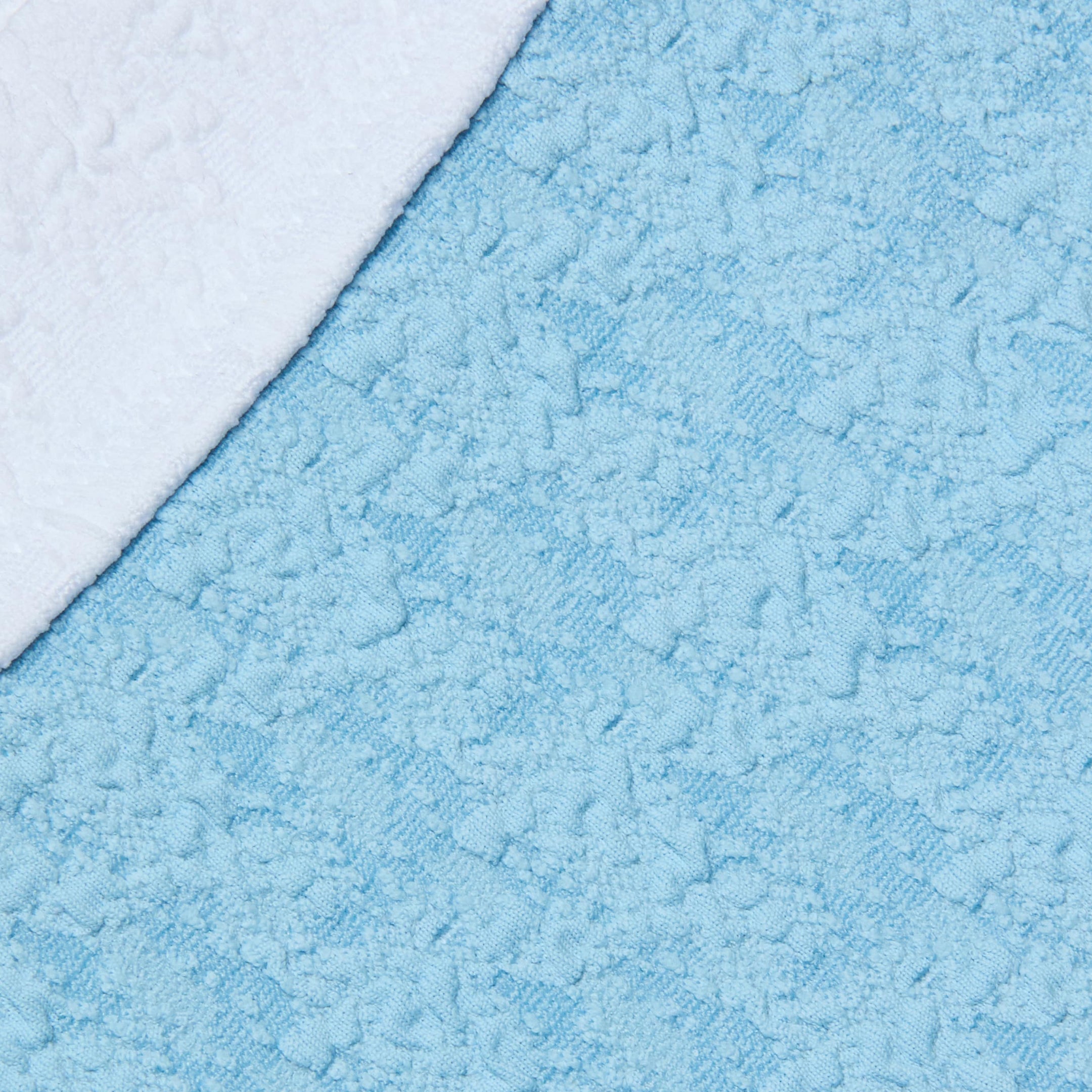 Close-up of the Jean Bikini Bottom in textured light blue bouclé swim fabric, with the curved corner of a white towel overlapping in the top left.