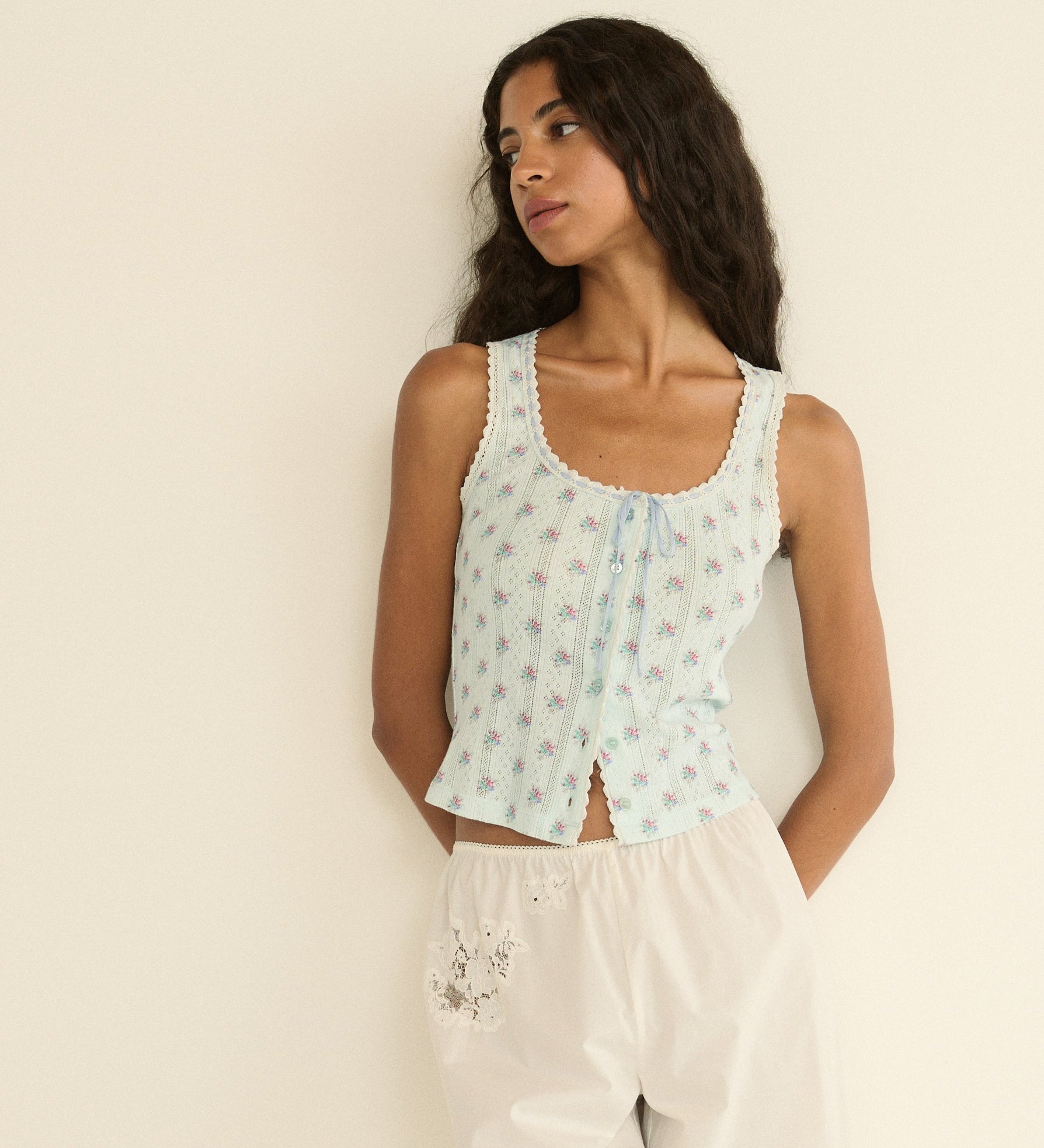 Woman wearing a light blue floral sleeveless top against a beige background