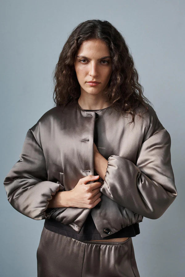 Woman wearing a gray satin jacket against a plain background