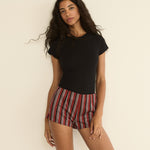 Woman wearing a black top and red striped shorts against a beige background