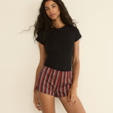 Woman wearing a black top and red striped shorts against a beige background