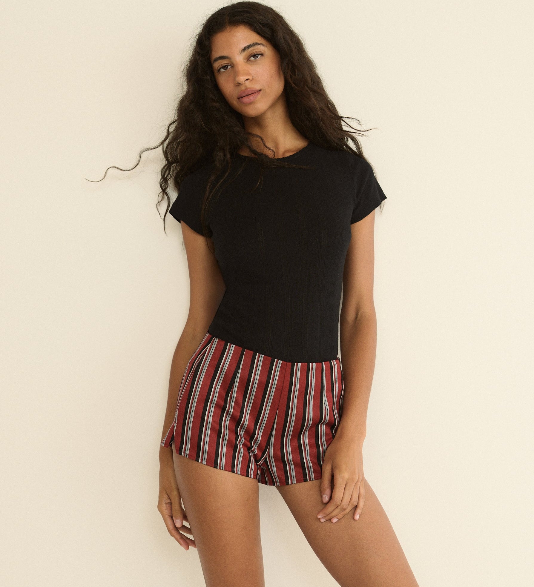 Woman wearing a black top and red striped shorts against a beige background