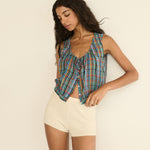 Woman wearing a plaid sleeveless top and beige shorts against a plain background