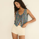 Woman wearing a plaid sleeveless top and beige shorts against a plain background