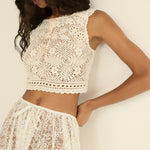 Woman wearing a white lace top and skirt against a plain background