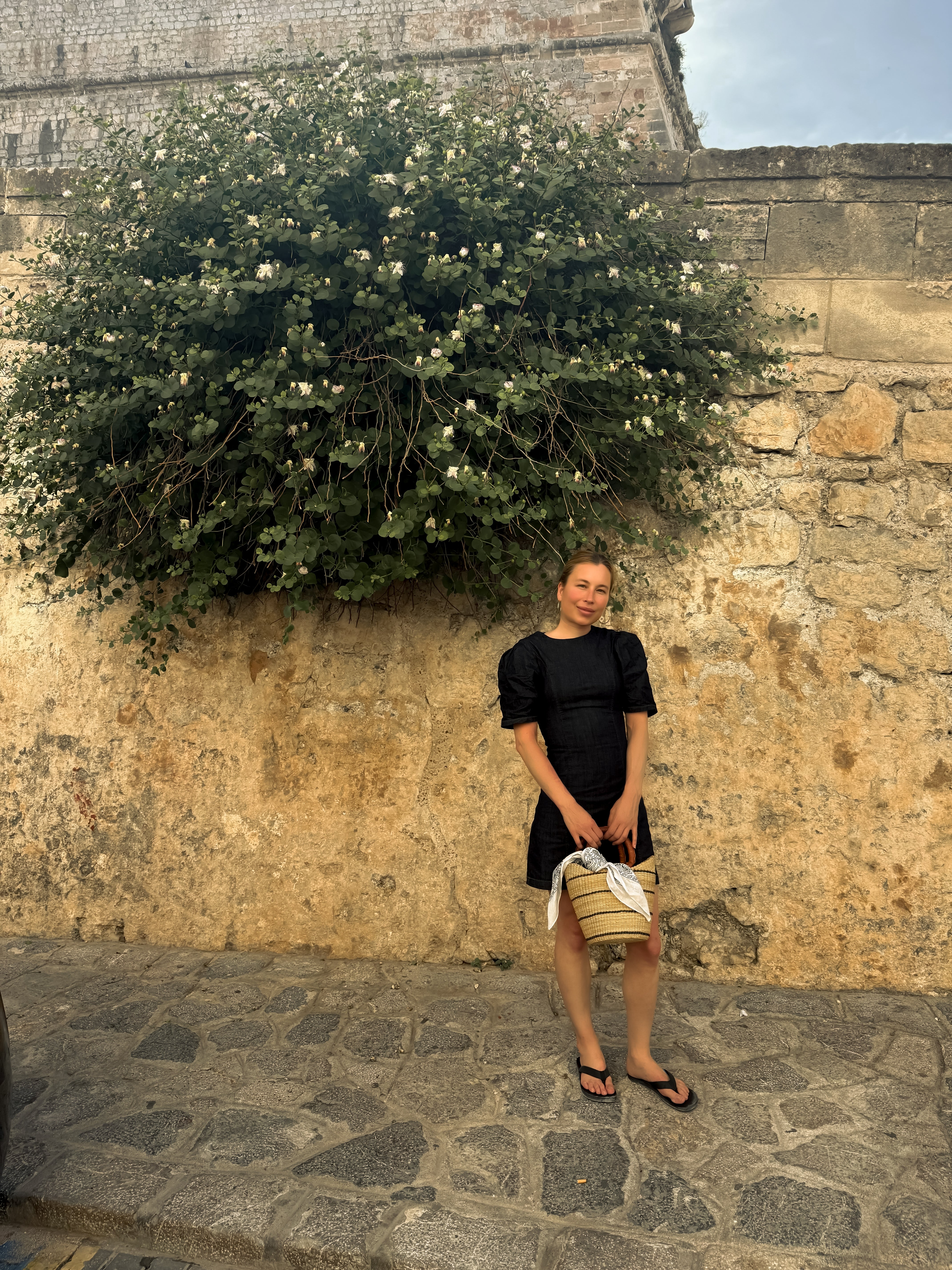 Woman in a black dress standing against a stone wall with greenery