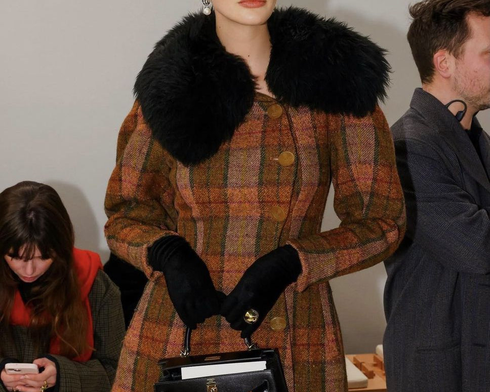 Model wearing a plaid coat with a fur collar at a fashion event.