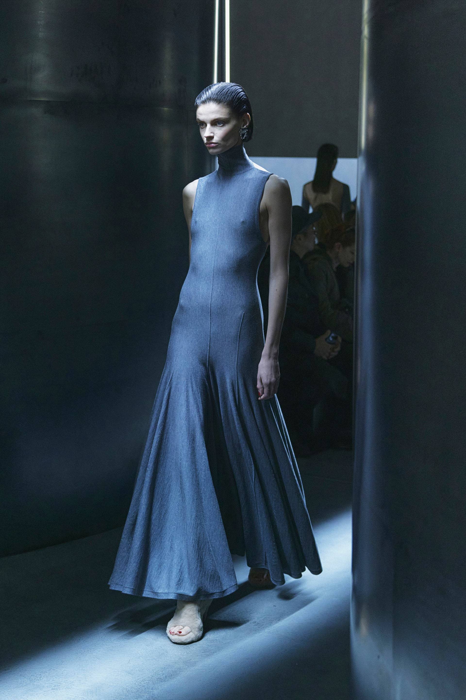 Woman in a blue dress standing in a dark room with a spotlight