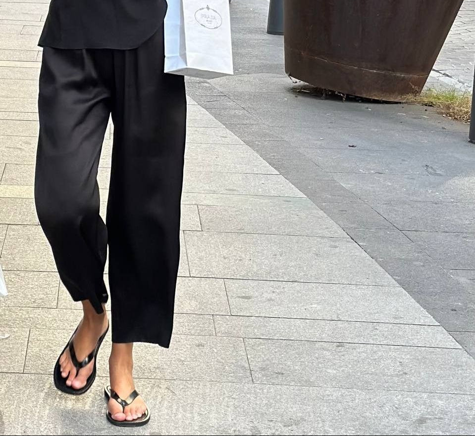 Person wearing a black outfit with sunglasses and a handbag on a city street.
