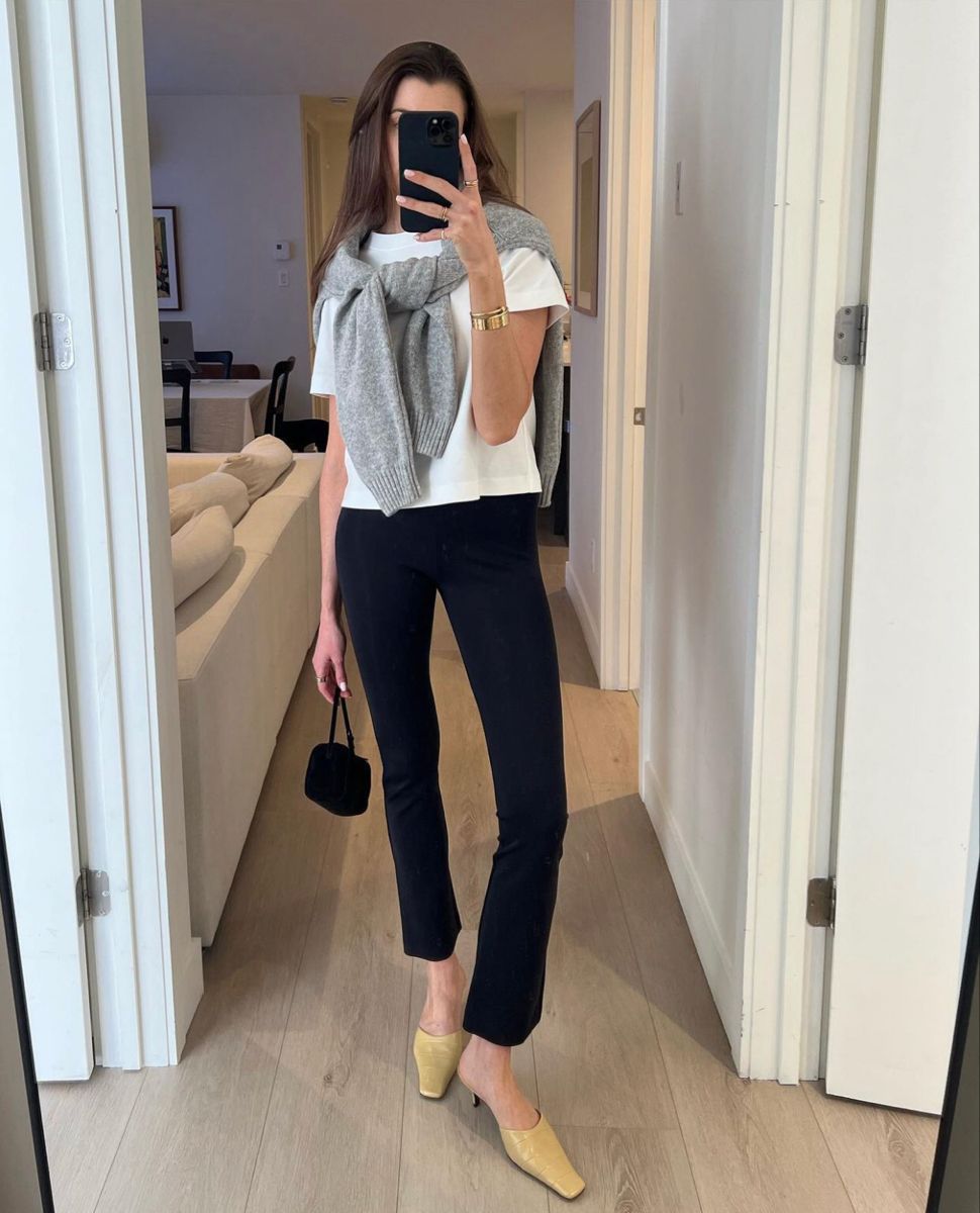 Woman taking a mirror selfie wearing a white top, black pants, and a gray scarf.