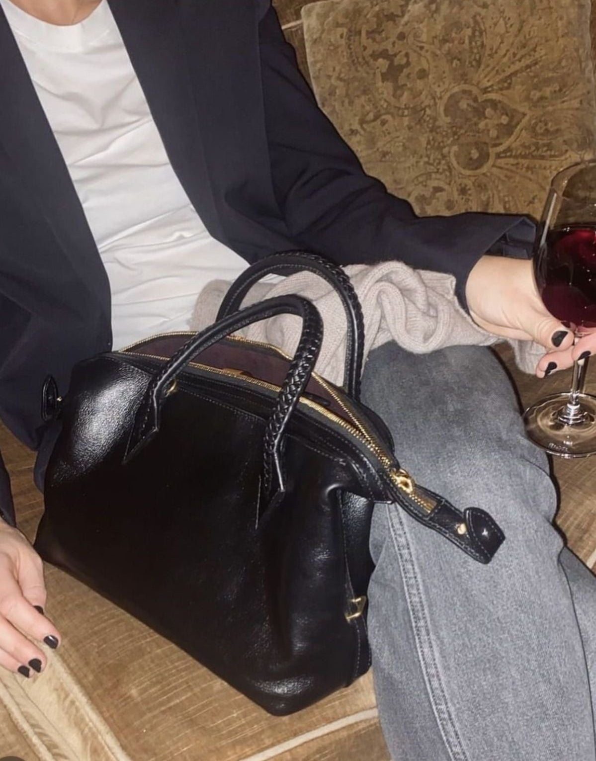 Person sitting on a couch with a black handbag and a glass of red wine.