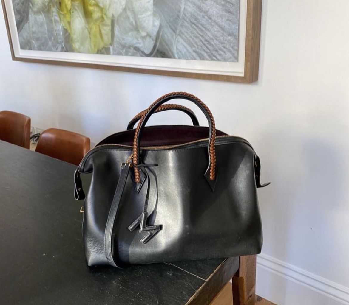 Black handbag with brown handles on a table in a room with a painting on the wall.