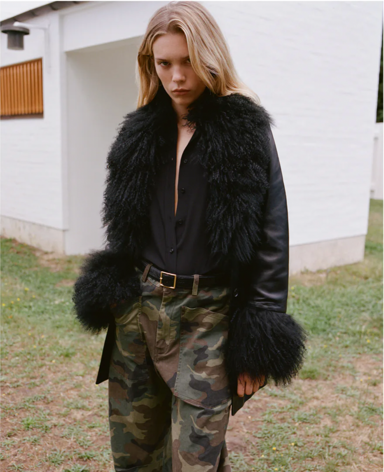 Person wearing a black fur coat and camouflage pants outdoors.