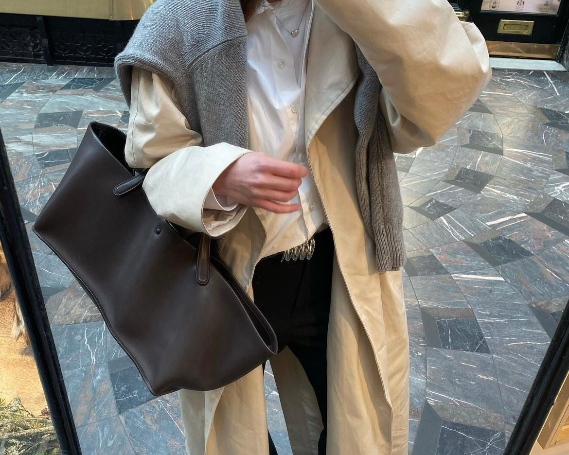 Person wearing a beige coat and holding a brown bag in a store setting
