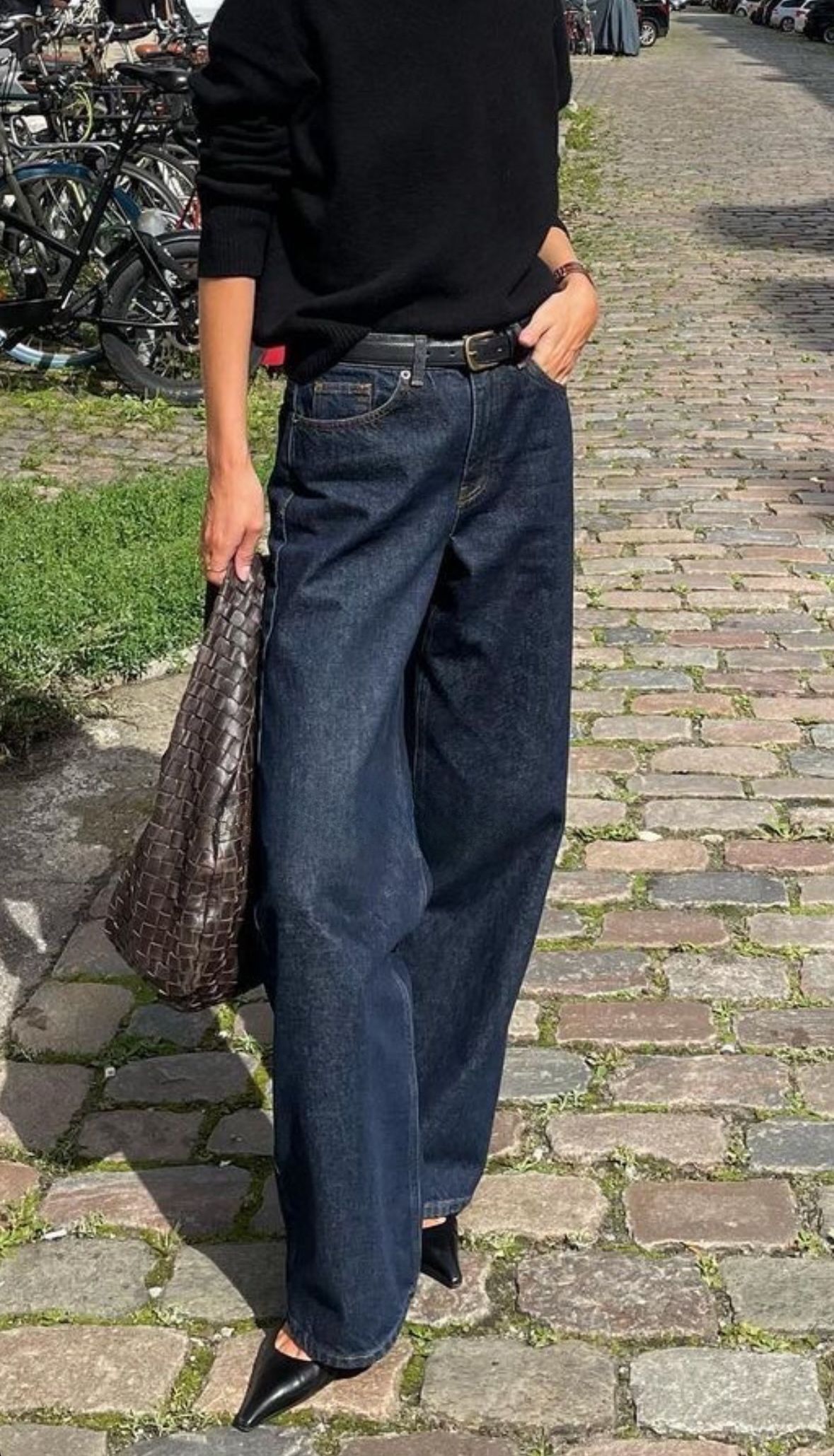 Person wearing a black sweater and blue jeans on a cobblestone street.