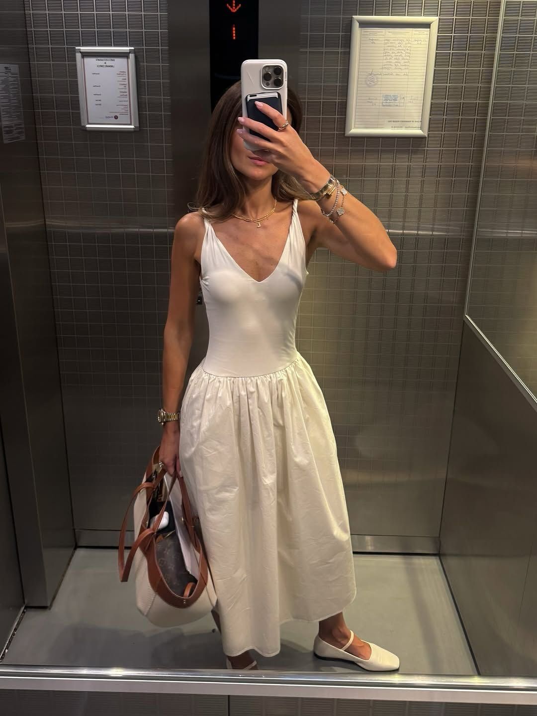 Woman taking a mirror selfie wearing a white dress in an elevator.