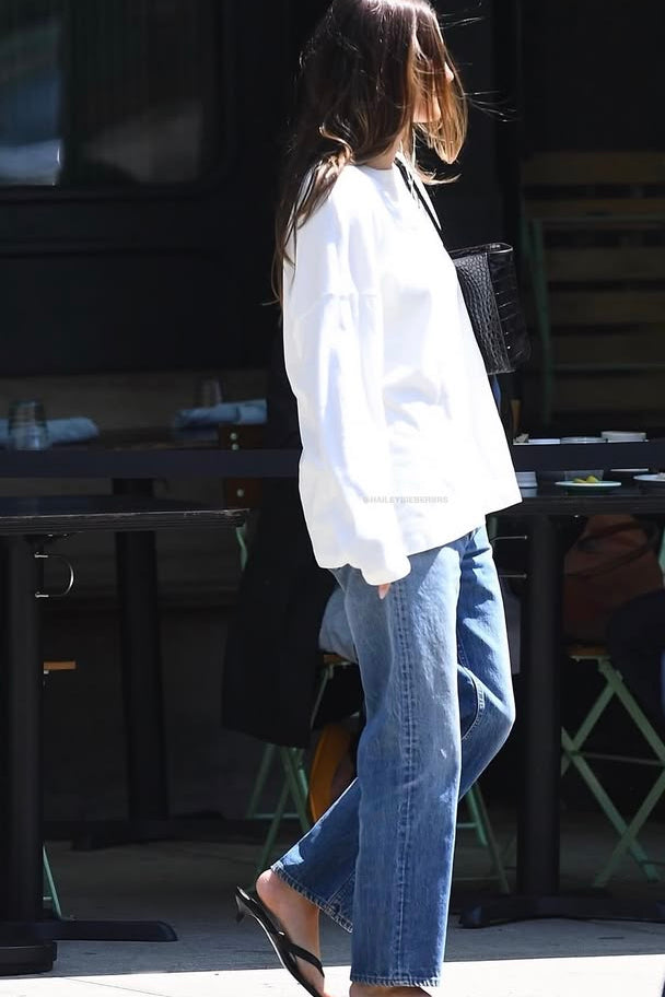 Person wearing a white jacket and blue jeans walking outdoors.