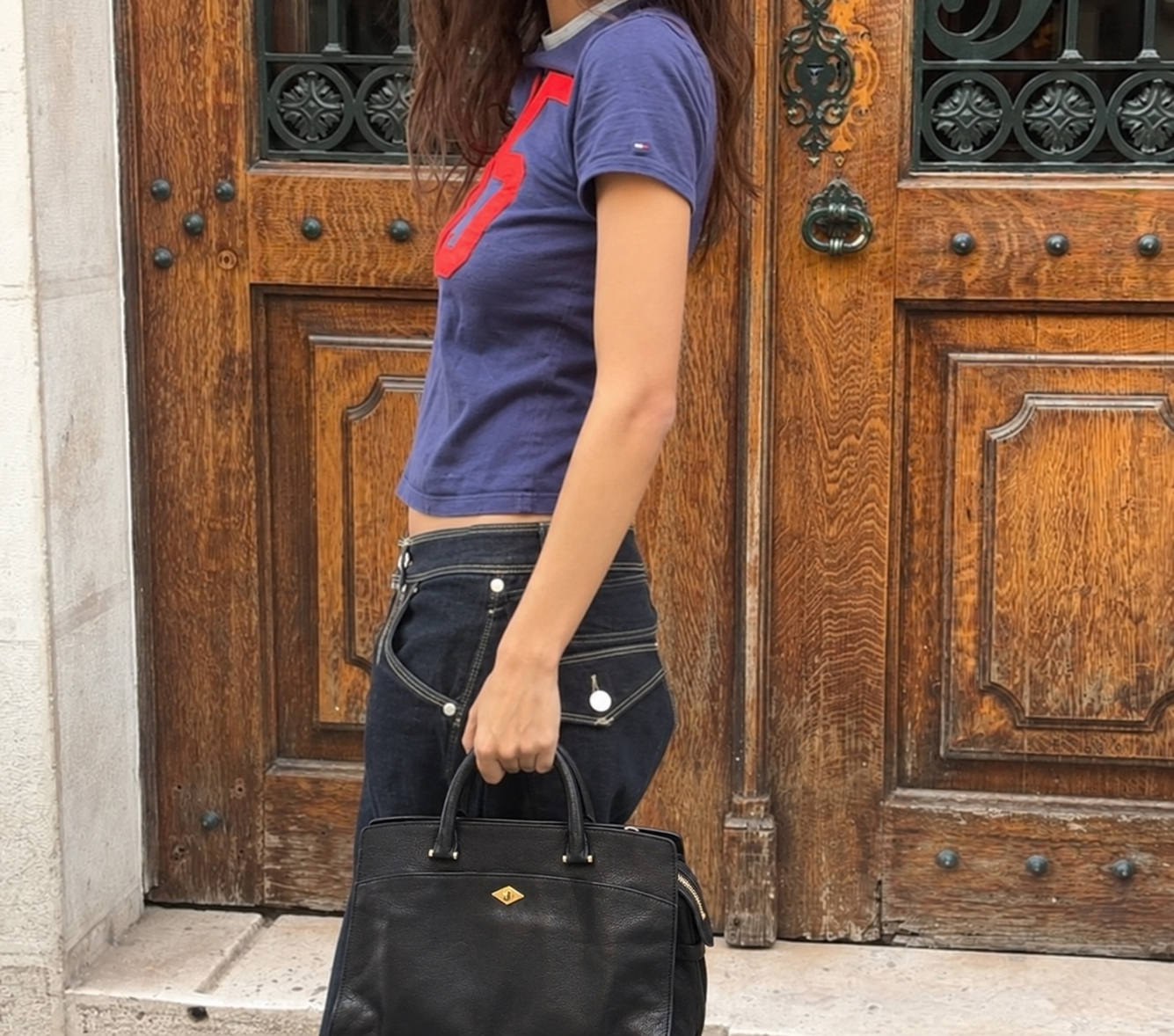 Black Private Eye held with a navy T-shirt and dark denim outside wooden doors